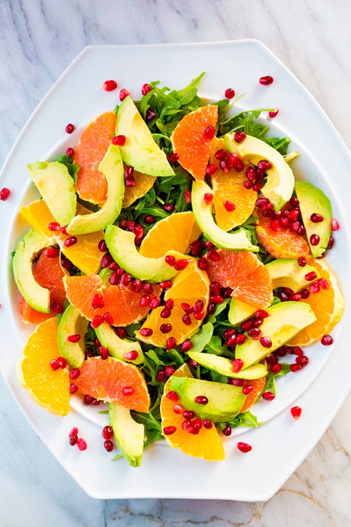 white bowl with arugula, slices of orange,avocado,grapefruit and pieces of pomegranate